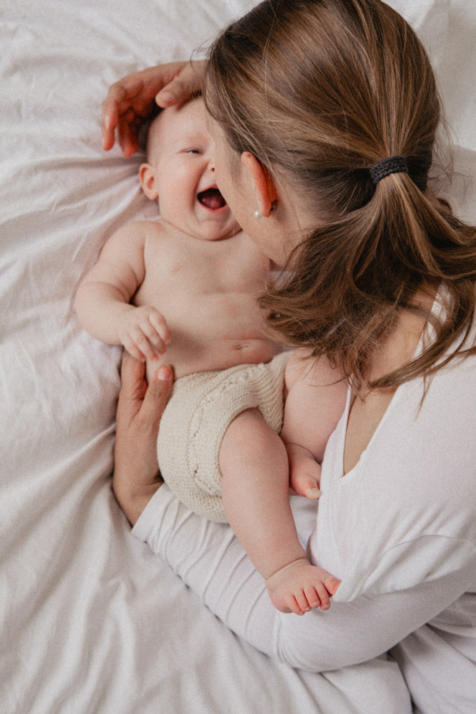 Familienfotografie Würzburg – Motherhood-Porträt: Mutter von hinten mit Baby auf dem Bett, persönliche Momente festgehalten.
