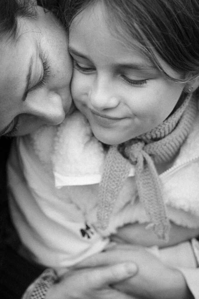 Schwarz-weiß Detailaufnahme: Mama küsst ihre Tochter liebevoll auf die Wange, inniger und emotionaler Familienmoment