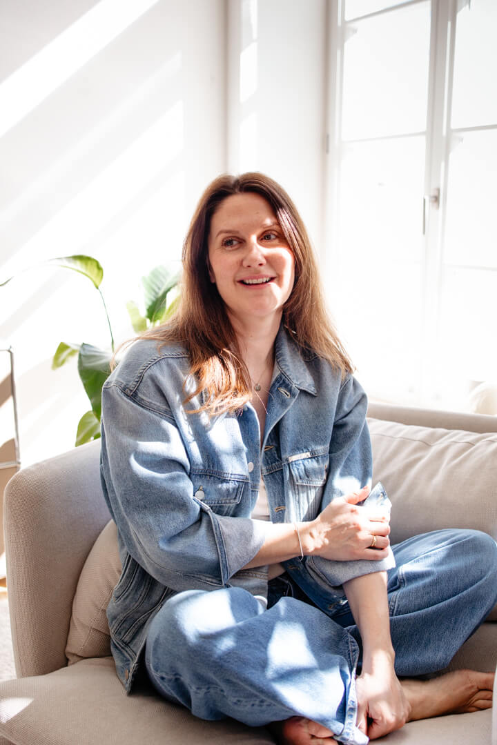 Natürliche Familienfotografin aus Würzburg: Fotografin Dorothee Moser im Schneidersitz sitzend auf einem Sessel bei schönem Tageslicht